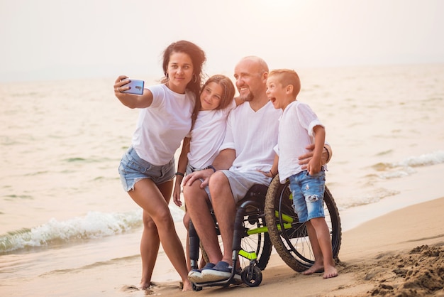 Homme handicapé en fauteuil roulant avec sa famille sur la plage.