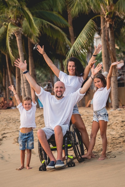 Homme handicapé en fauteuil roulant avec sa famille sur la plage.