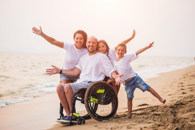 Homme handicapé en fauteuil roulant avec sa famille sur la plage.