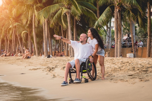Homme handicapé en fauteuil roulant avec sa femme sur la plage.