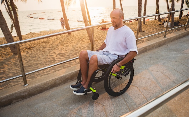 Homme handicapé en fauteuil roulant se déplace sur une rampe d'accès à la plage.