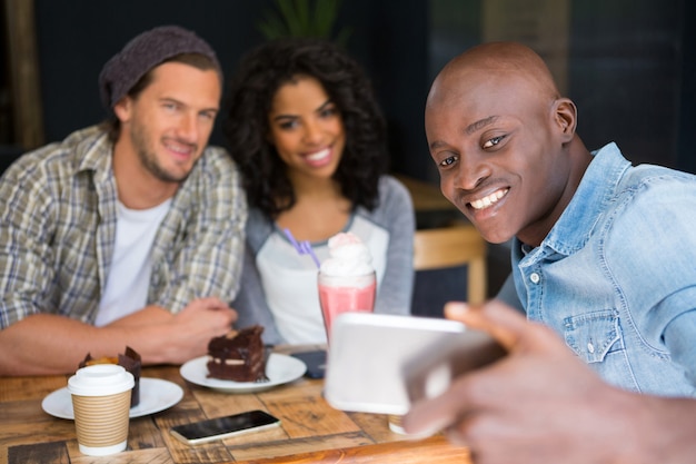 Homme heureux avec des amis prenant selfie à table en bois dans un café