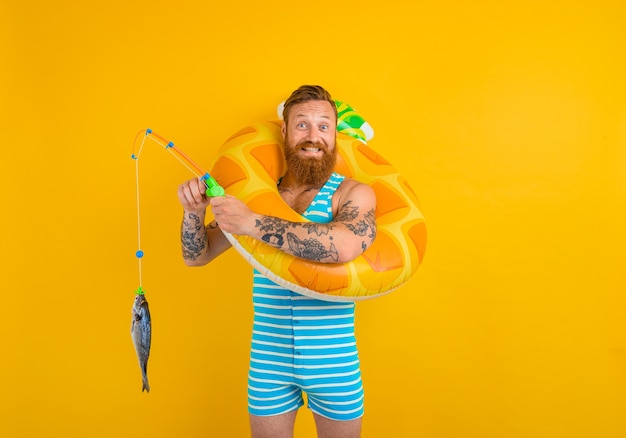 Un homme heureux avec une barbe et un beignet gonflable attrape du poisson