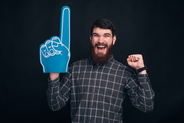 Homme heureux avec barbe célébrant la victoire et pointant avec un gant de fan