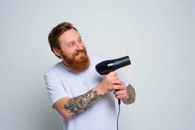 Un homme heureux avec une barbe joue avec un sèche-cheveux