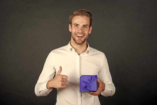 Homme heureux avec boîte enveloppée sur fond noir montrant le pouce vers le haut le lendemain de Noël