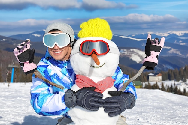 Homme heureux avec bonhomme de neige à la station de ski. Vacances d'hiver