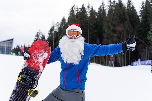 homme heureux en bonnet de noël rouge avec snowboard à la colline des montagnes d'hiver.