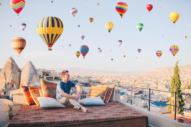 Homme heureux en Cappadoce. Jeune homme sur un toit avec des ballons à air en arrière-plan dans le ciel bleu à Göreme en Cappadoce, Turquie