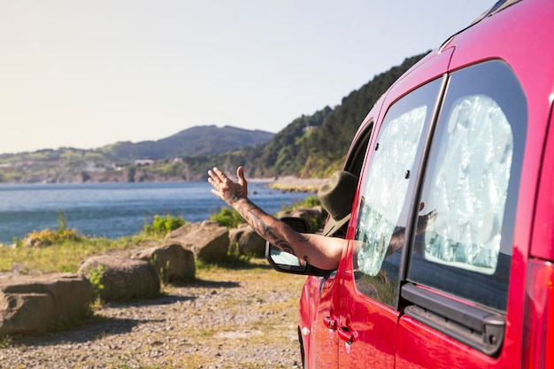 Un homme heureux conduit un camping-car et passe sa main par la fenêtre Voyage en bord de mer et concept de liberté