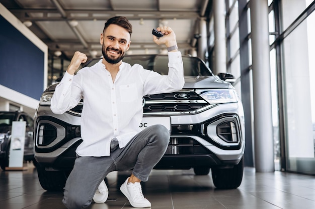 Homme heureux debout devant une nouvelle voiture dans une salle d'exposition de voitures