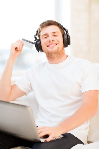 homme heureux avec des écouteurs et une carte de crédit écoutant de la musique à la maison