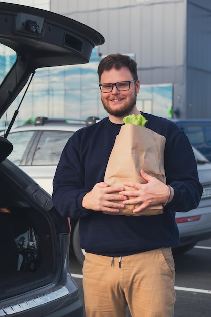 L'homme heureux a mis le sac d'épicerie dans le coffre de la voiture, dans le parking du centre commercial.