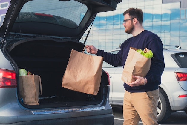 L'homme heureux a mis le sac d'épicerie dans le coffre de la voiture, dans le parking du centre commercial.