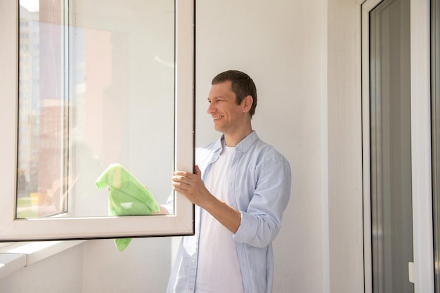 Un homme heureux nettoie la maison Laver les fenêtres avec un chiffon sur le balcon