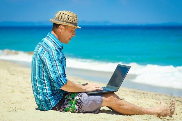 Un homme heureux avec un ordinateur portable près du voyage de week-end au bord de la mer