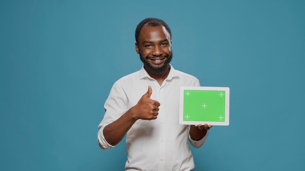 Homme heureux pointant vers une tablette numérique avec écran vert horizontal à la main, espace de copie isolé montré avec modèle de clé chroma vierge et arrière-plan maquette. Technologie d'affichage moderne.