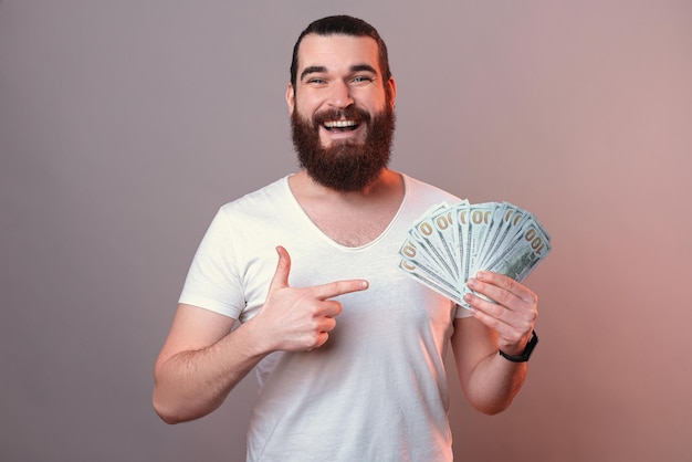 Un homme heureux pointe du doigt le tas d'argent qu'il tient Studio shot