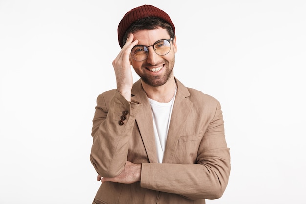 homme heureux portant un chapeau hipster souriant et touchant son front isolé sur un mur blanc