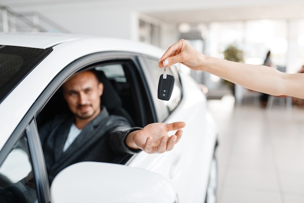 Un homme heureux prend la clé de la nouvelle voiture dans la salle d'exposition.