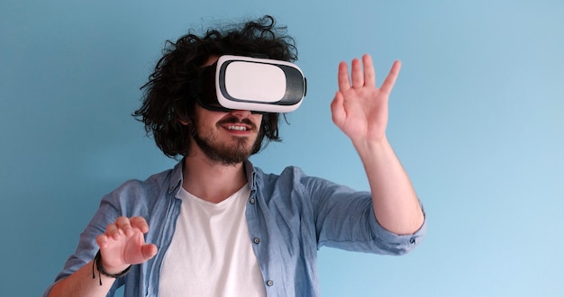 Un homme heureux qui acquiert de l'expérience à l'aide de lunettes de casque VR de réalité virtuelle, isolé sur fond bleu