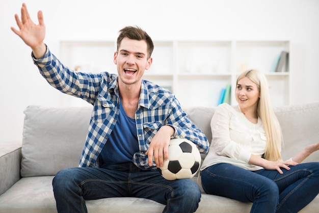 L'homme heureux regarde un football et fait un geste près de la femme sur le canapé