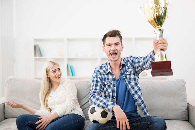 L'homme heureux regarde un football et fait un geste près de la femme sur le canapé