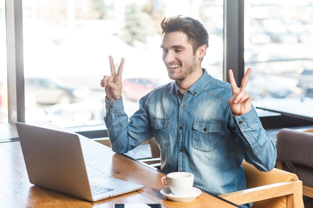 Photo homme heureux souriant travaillant sur un ordinateur portable a un appel vidéo montrant le signe v à scree se réjouit de sa victoire