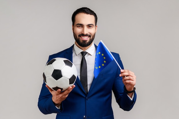 Un homme heureux tient un ballon de football noir et blanc et un drapeau de l'UE regardant l'équipe préférée de soutien au football