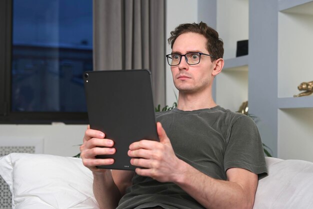 Un homme heureux utilise une tablette à la maison en regardant l'écran et assis sur un canapé dans le salon