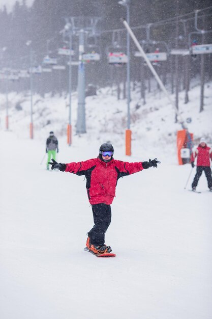 Homme heureux en veste rouge sur le ski de snowboard sur la montagne Il neige