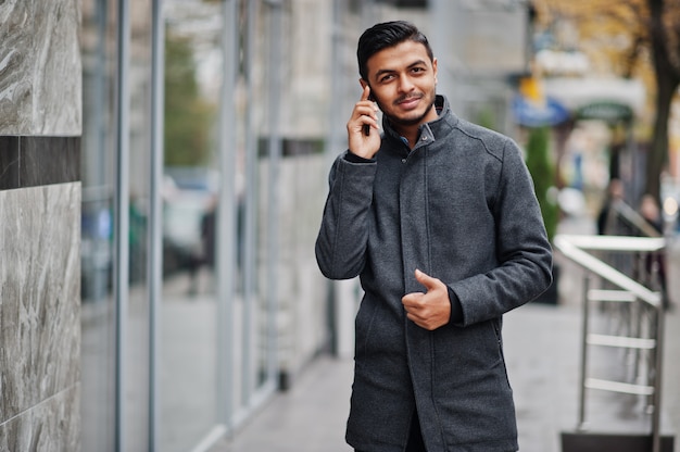 Homme hindou élégant en manteau gris posé dans la rue et parlant au téléphone