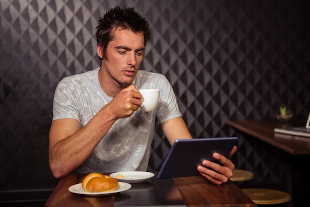 Homme de hipster à l'aide de tablette avec café et pâtisserie