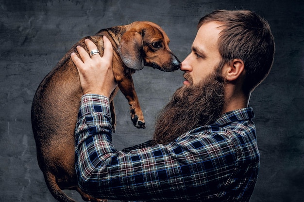 Homme hipster barbu dans une chemise à carreaux bleue tient dans les bras un chien blaireau brun.