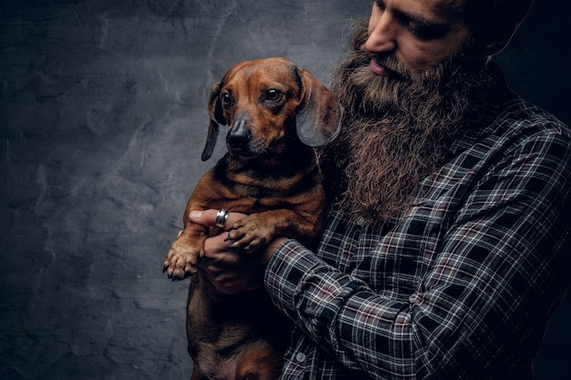 Homme hipster barbu dans une chemise à carreaux bleue tient dans les bras un chien blaireau brun.