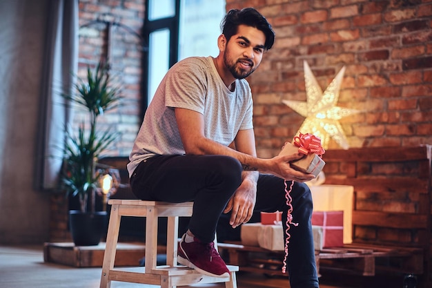 Homme hipster barbu indien avec des tatouages sur le bras dans une chambre loft avec décoration de Noël.