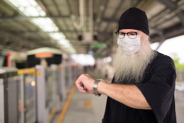 Homme Hipster Barbu Mature Avec Masque Pour La Protection Contre L'épidémie De Virus Corona Vérifier L'heure à La Gare