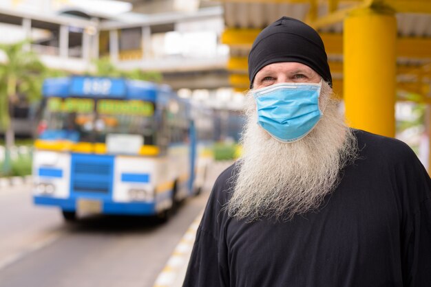 Homme hipster barbu mature portant un masque pour se protéger contre l'épidémie de virus corona et la pollution à l'arrêt de bus