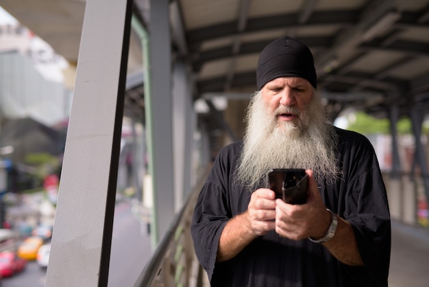 Homme hipster barbu mature a souligné à l'aide de téléphone et à la passerelle choquée dans la ville