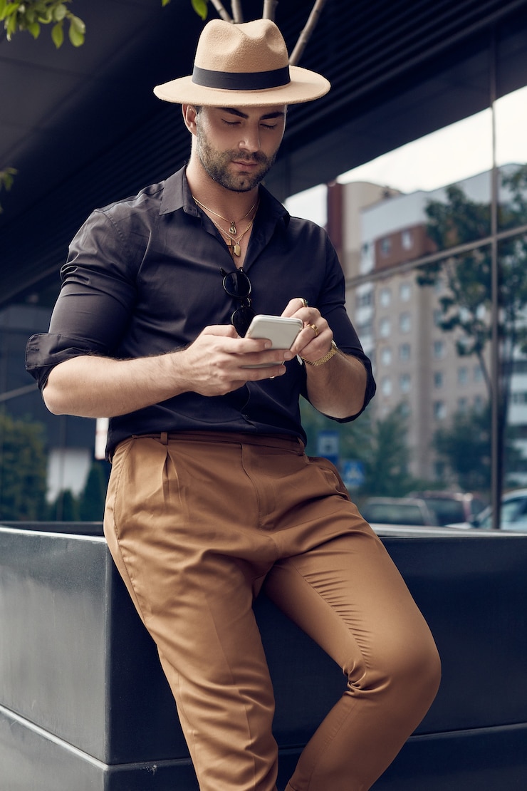 Photo homme de hipster musclé tanné brutal en chemise noire et un chapeau avec téléphone