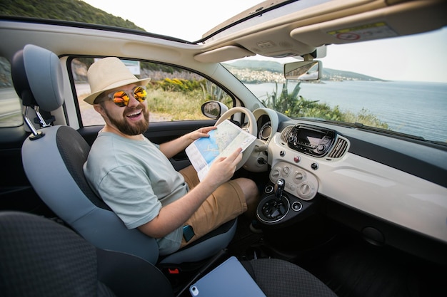 Homme hipster regardant sur la carte de navigation de localisation dans le voyageur de tourisme de voiture conduisant et tenant dans la main masculine