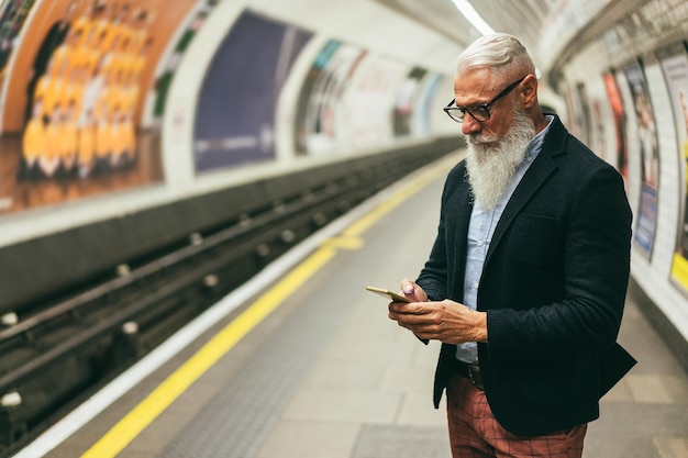 Homme hipster senior utilisant un smartphone dans le métro souterrain L'accent principal est mis sur la main tenant le téléphone portable