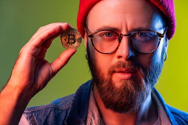 Homme hipster tenant dans les doigts montrant une pièce d'or bitcoin monnaie crypto monnaie virtuelle électronique