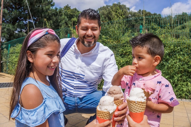 Homme hispanique adulte mangeant la crème glacée avec ses enfants en parc