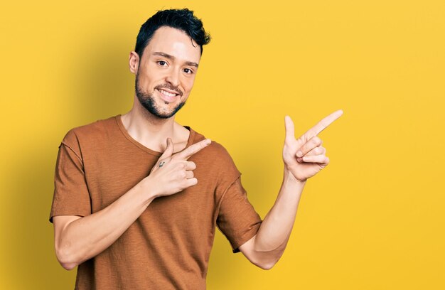 Homme hispanique avec barbe portant un t-shirt décontracté souriant et regardant la caméra pointant avec deux mains et doigts sur le côté