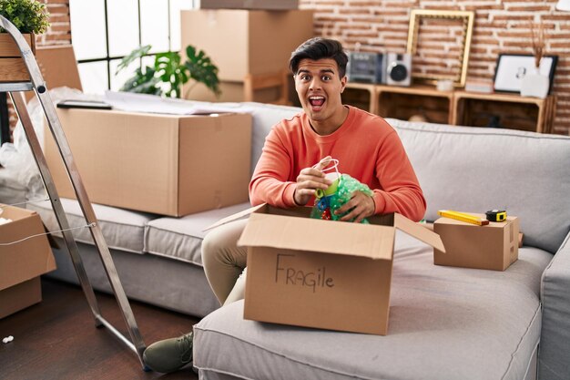 Photo homme hispanique déménageant dans une nouvelle maison déballant célébrant fou et étonné du succès avec les yeux ouverts criant excité