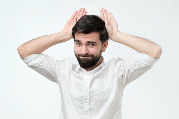 Homme hispanique drôle mignon avec des barbes se tenant la main près de la tête comme des oreilles d'animaux