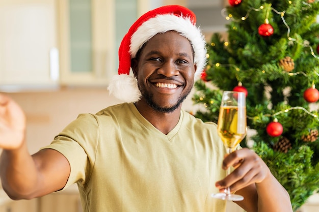 Homme hispanique latin en bonnet de noel parlant par connexion vidéo avec une coupe de champagne à la maison