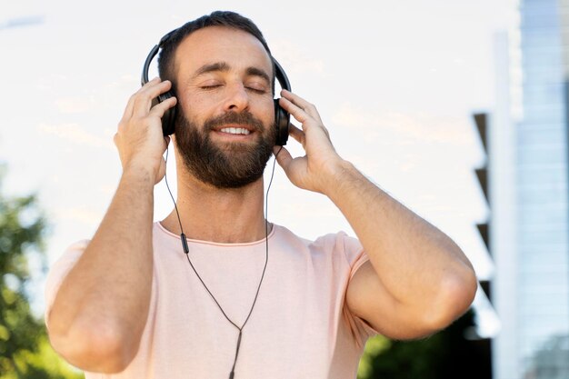 Homme hispanique souriant écoutant de la musique les yeux fermés debout dans la rue