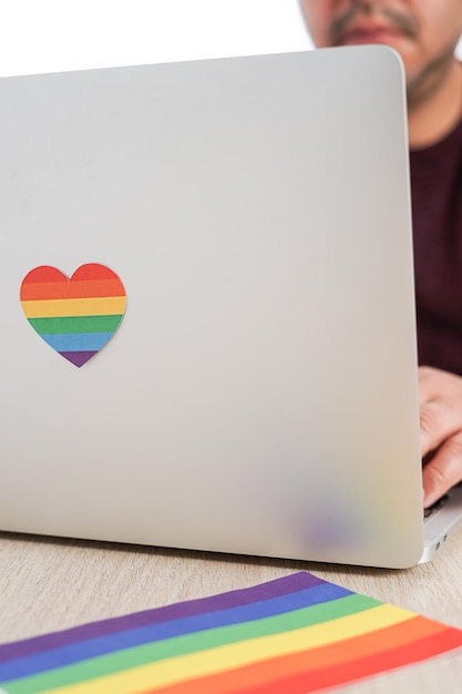 Homme hispanique travaillant avec son ordinateur qui a un cœur et un drapeau aux couleurs LGBTQ